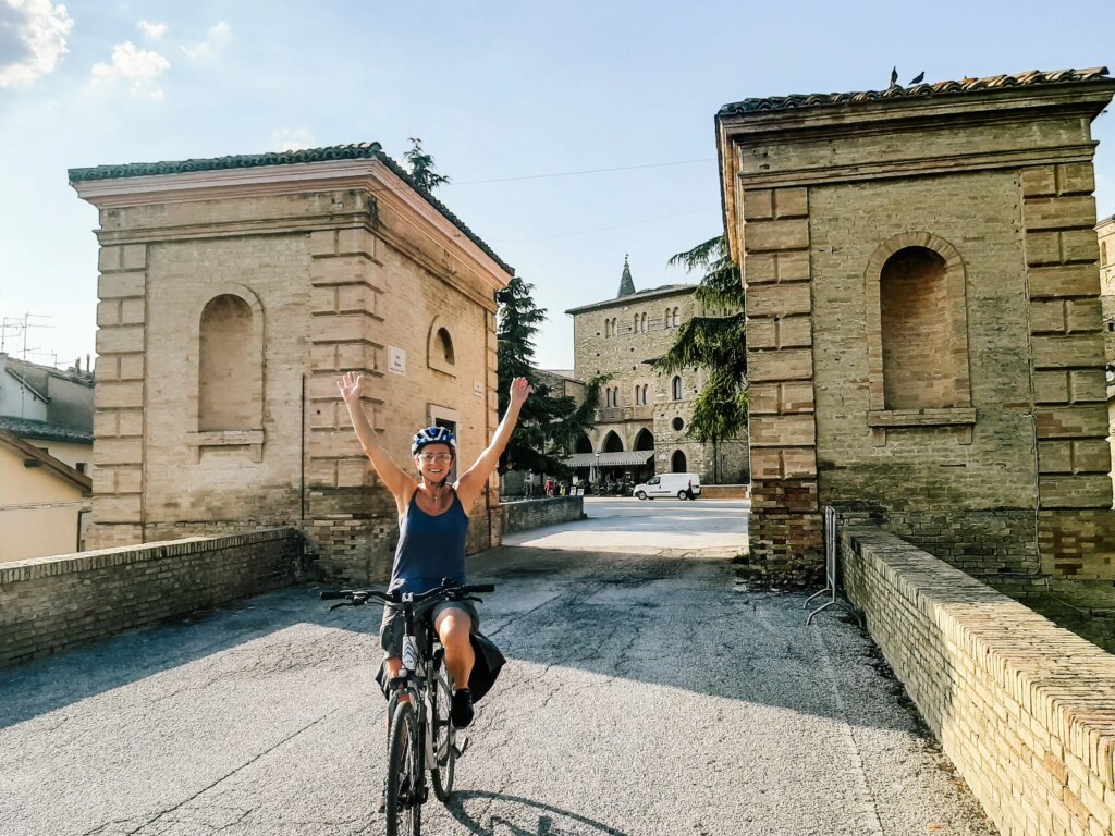 Cyclist crossing a historic stone bridge in Bevagna, Umbria. Travel by Girolibero.