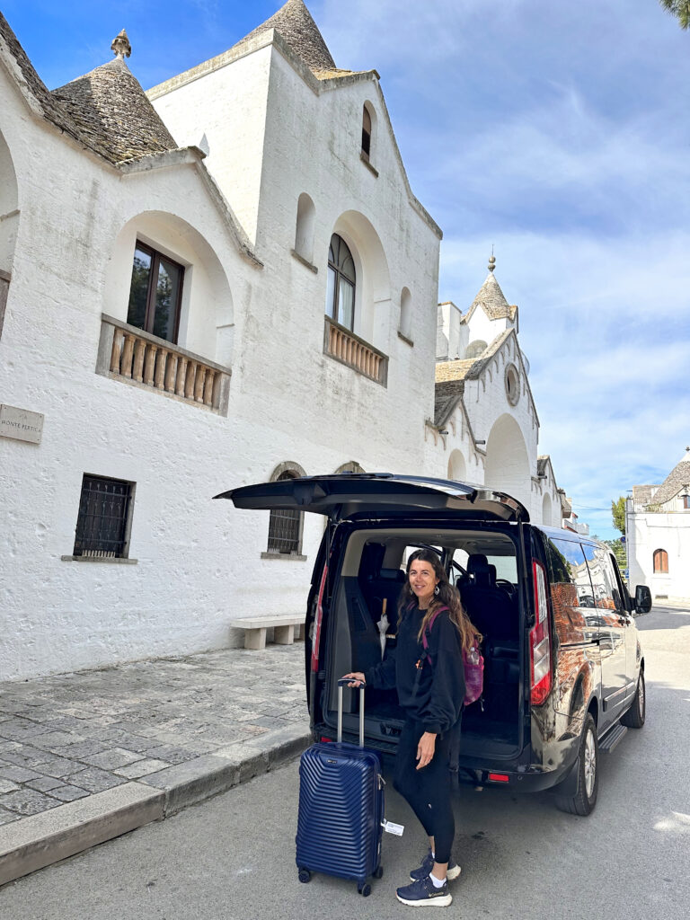 People loading luggage into a van on a cobblestone street near white houses.